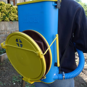 Person holding a blue and yellow backpack sprayer outdoors.
