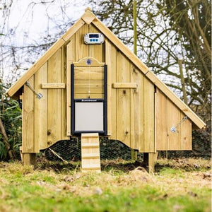 Wooden chicken coop with an automatic door on a grassy area with trees in the background