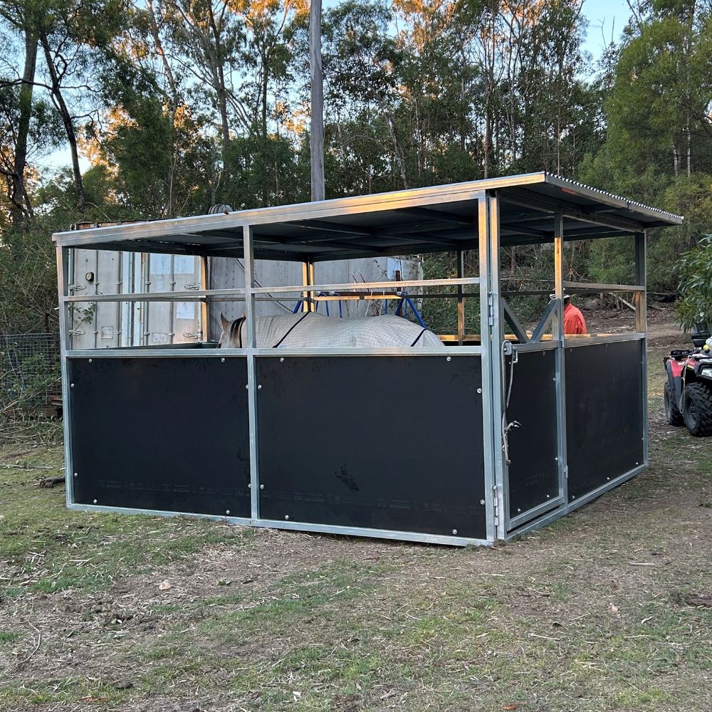 Large metal and black panel structure outdoors with a horse in it and trees in the background