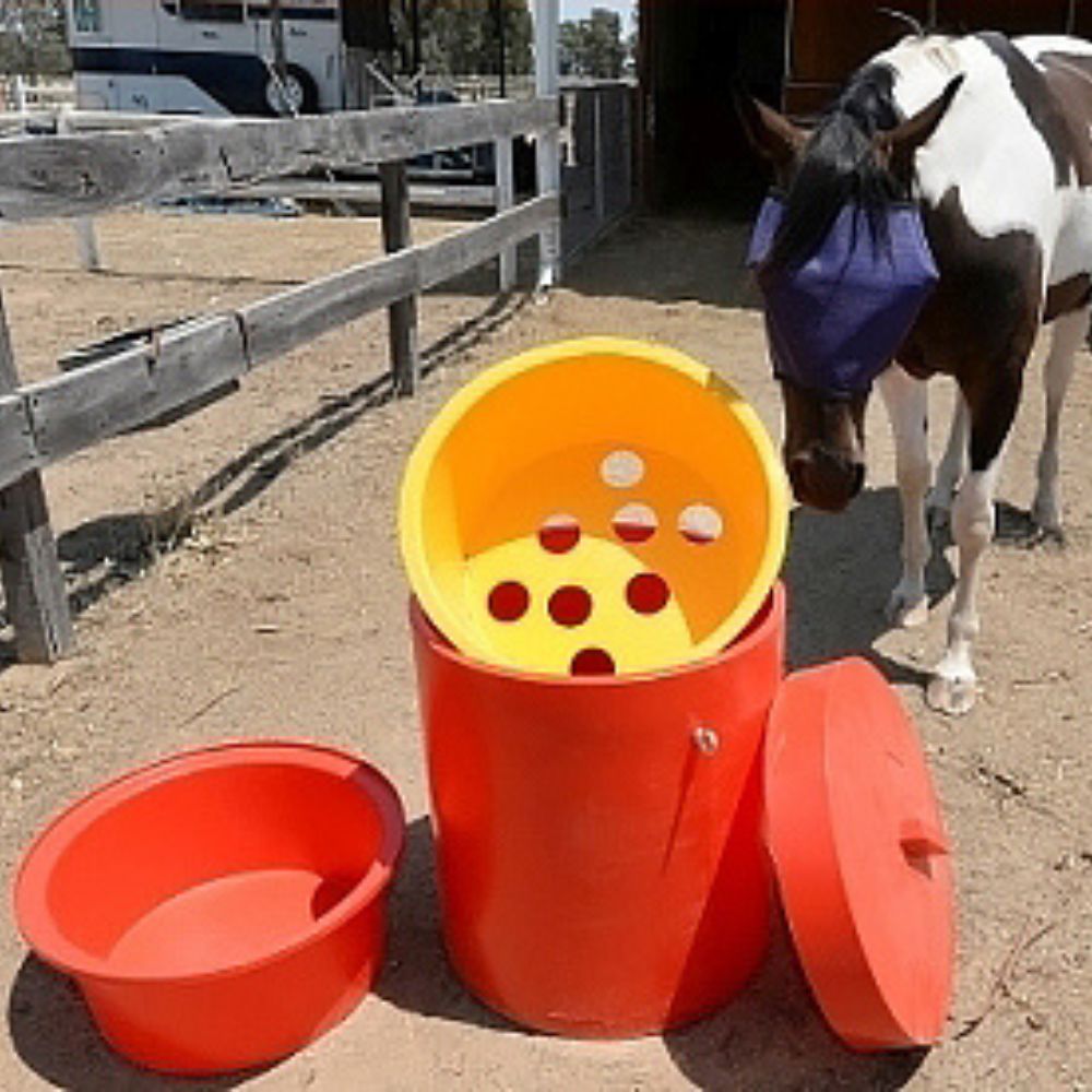 Red and yellow bucket with holes, next to a horse in a stable.