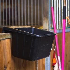 Black plastic feed trough attached to a wooden wall in a stable setting.