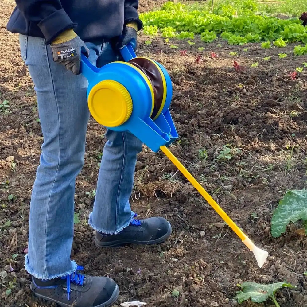 Person holding a blue and yellow bellows duster in a garden setting