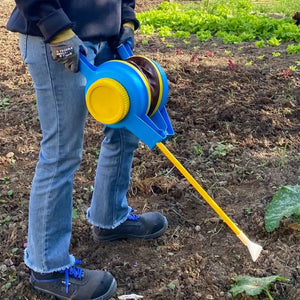 Person holding a blue and yellow bellows duster in a garden setting