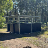 Outdoor horse stable with a black base and steel top, surrounded by trees.