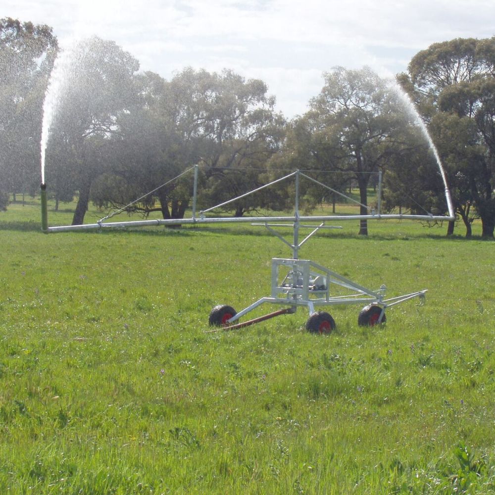 Farm irrigator system watering a grassy field with trees in the background