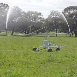 Farm irrigator system watering a grassy field with trees in the background