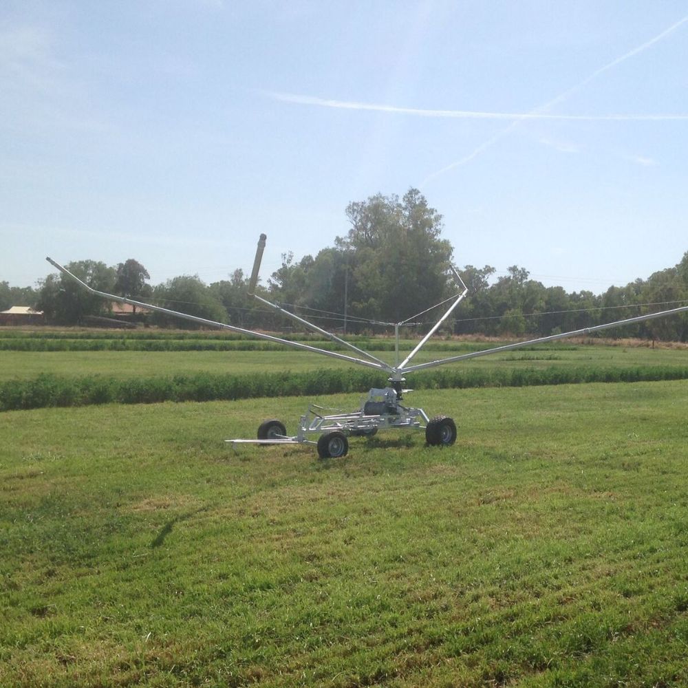 Farm irrigator system watering a grassy field with trees in the background