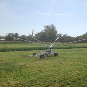 Farm irrigator system watering a grassy field with trees in the background