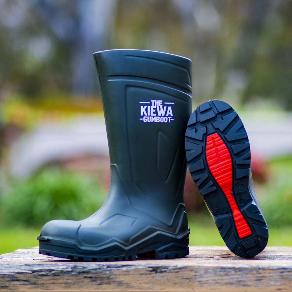 Dark green gumboot with red sole on a wooden surface, blurred green background