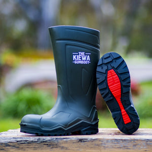 Dark green gumboot with red sole on a wooden surface, blurred green background