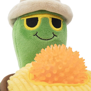 Green plush toy with a smiling face, wearing a white hat and sitting on an orange cushion.