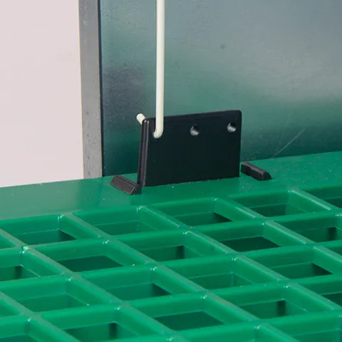 Green grid-like treadle surface of a metal and plastic bird feeder with green base and top on a white background.