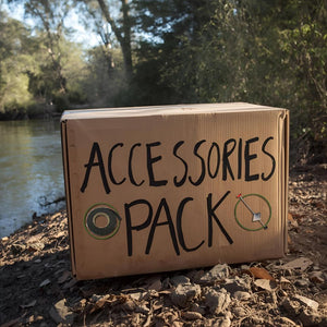 Cardboard box labeled 'Accessories Pack' by a river with trees in the background