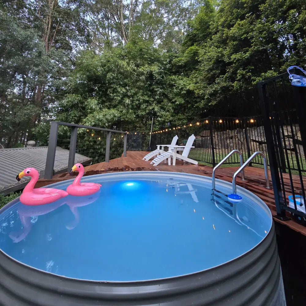 Above-ground pool with pink flamingo floats in a backyard setting with trees and deck chairs.